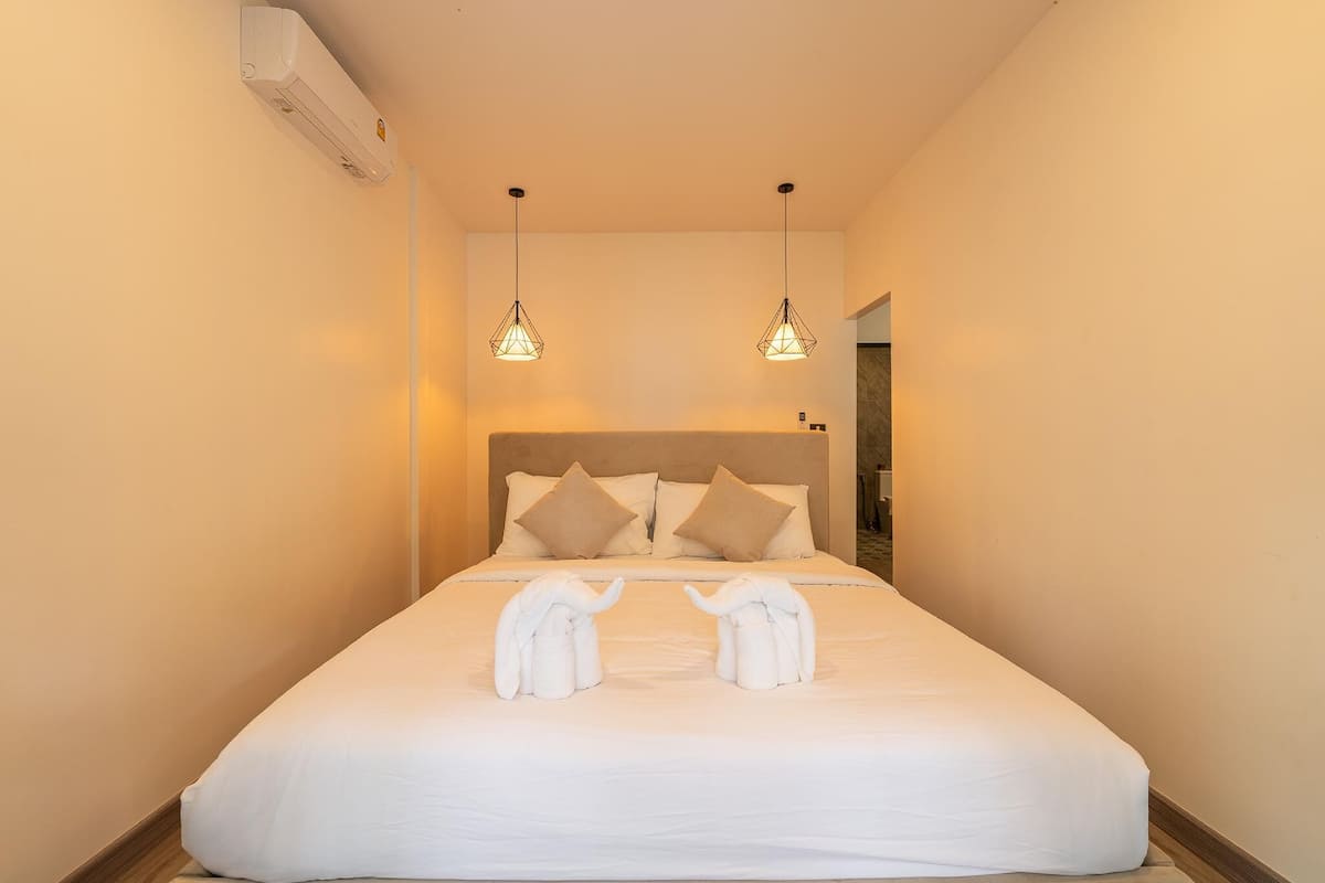 A hotel room with a large bed, two hanging pendant lights, and a headboard with pillows.
