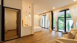 A spacious room with a wooden floor, a bed, a sofa, and a large window with curtains. - Inthada At Mae Kampong Chiang Mai (Mae On)