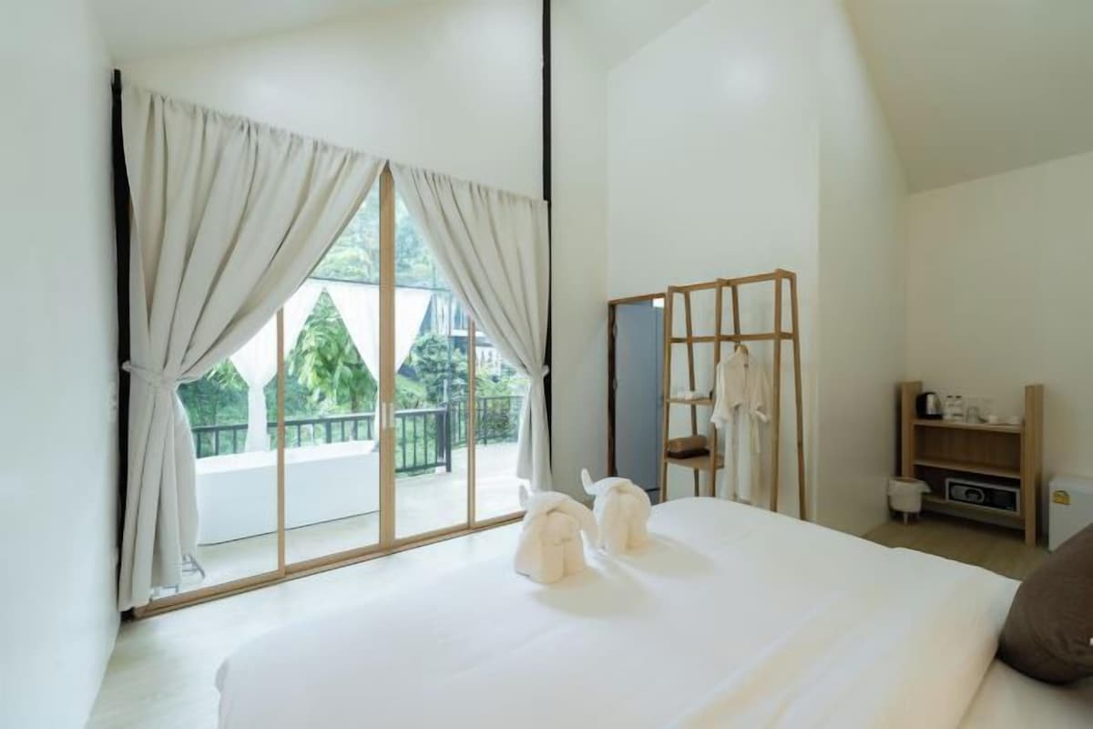 A hotel room with a large bed, a wardrobe, a mirror, and a view of greenery outside.