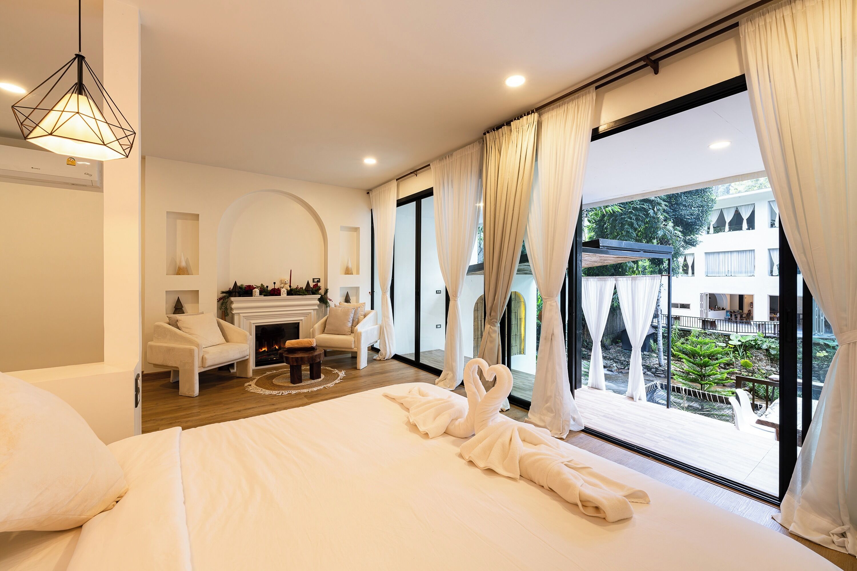 Una habitación de hotel moderna con una cama grande, una chimenea, una zona de estar con un sofá y sillones, y un balcón con vistas a los alrededores.