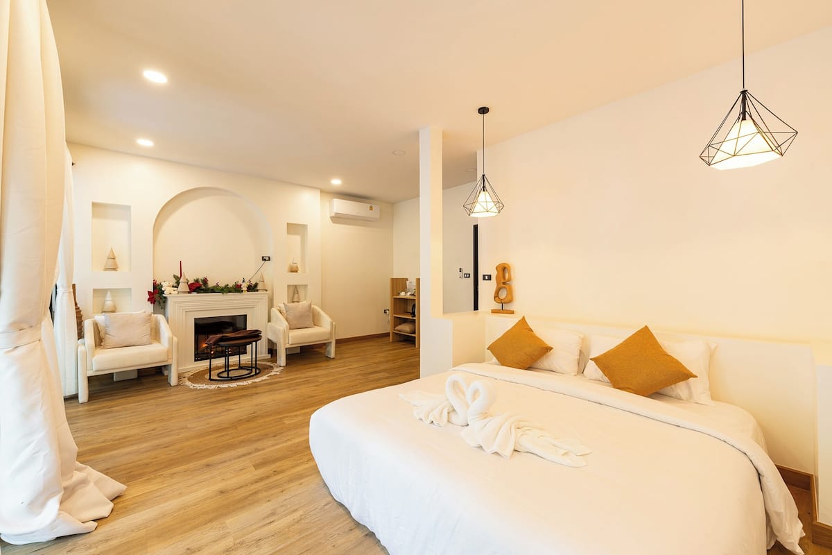 A modern hotel room with a large bed, a fireplace, a seating area with chairs, and a hanging light fixture.