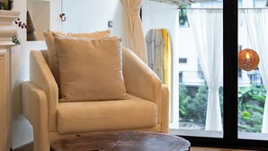 A modern living room with a beige armchair, a round wooden coffee table, and a large window with sheer curtains. - Inthada At Mae Kampong Chiang Mai (Mae On)
