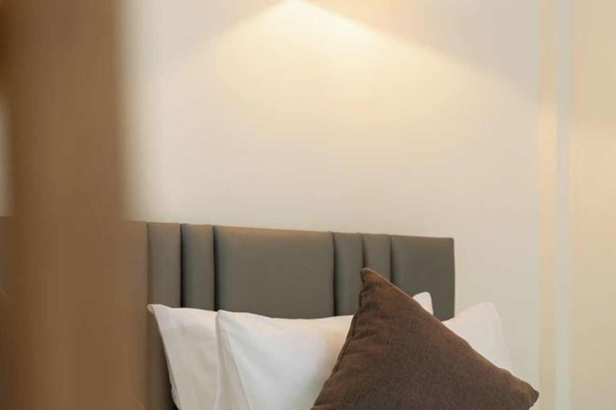 A hotel room with a bed featuring a grey upholstered headboard and white and brown pillows.