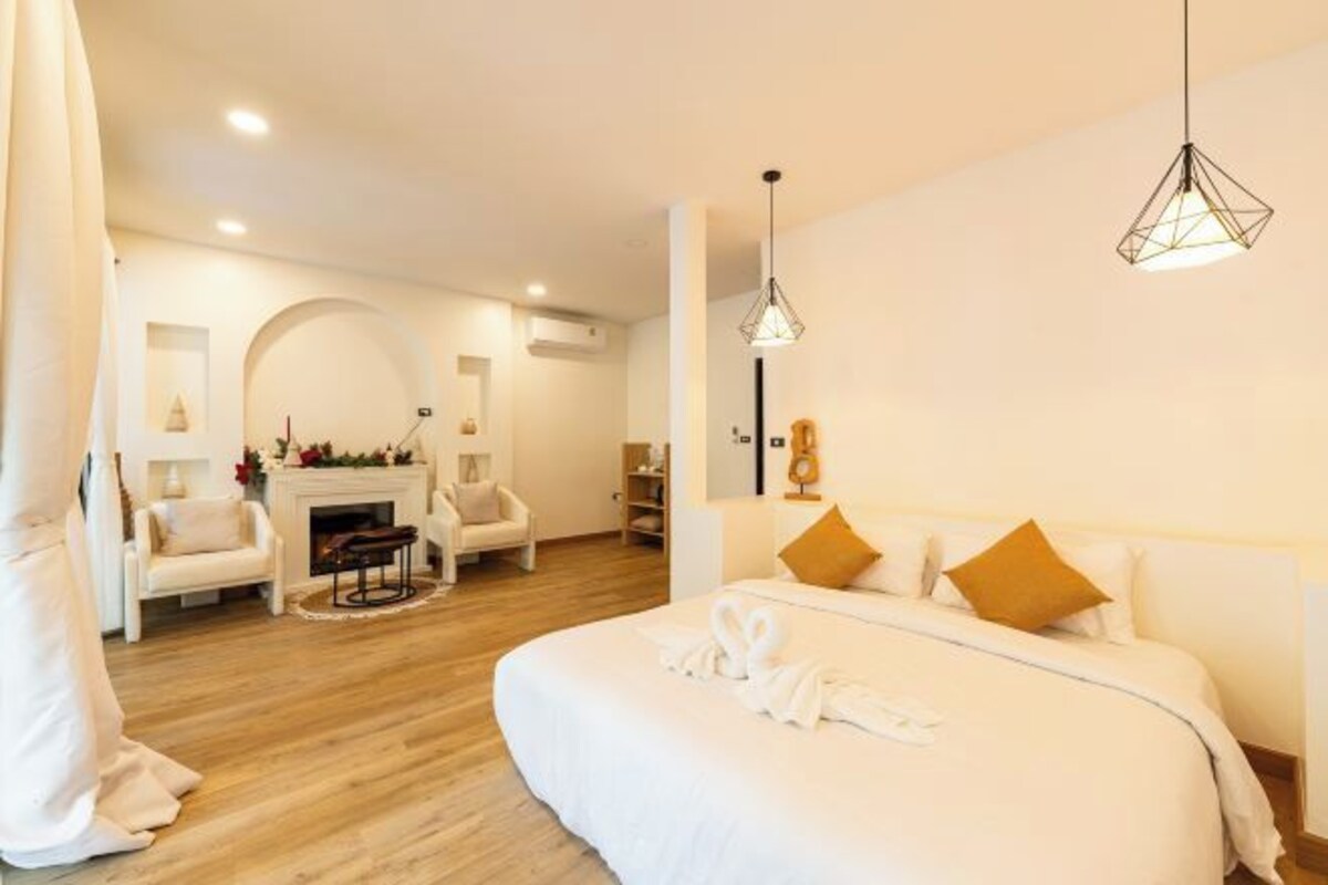 A modern hotel room with a large bed, a fireplace, and a seating area with chairs.