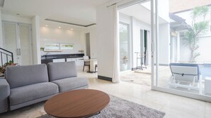 A modern living room with a grey sofa, a round coffee table, and a sliding glass door leading to a balcony with a pool.
