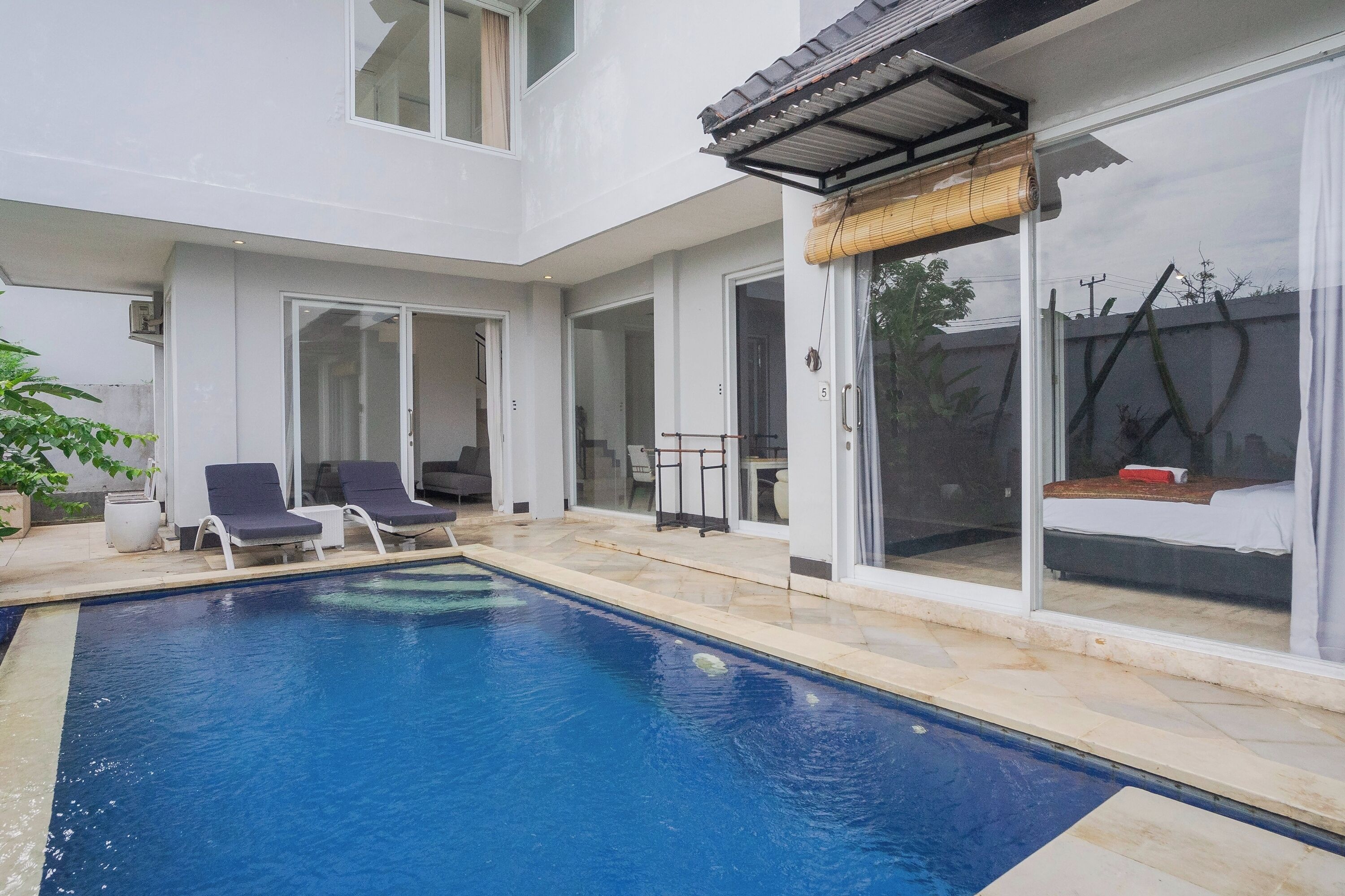 A modern house with a swimming pool, a covered patio, and a sliding glass door leading to a bedroom.