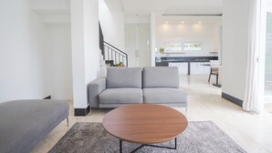 A modern living room with a grey sofa, a round wooden coffee table, and a staircase leading to an upper floor.