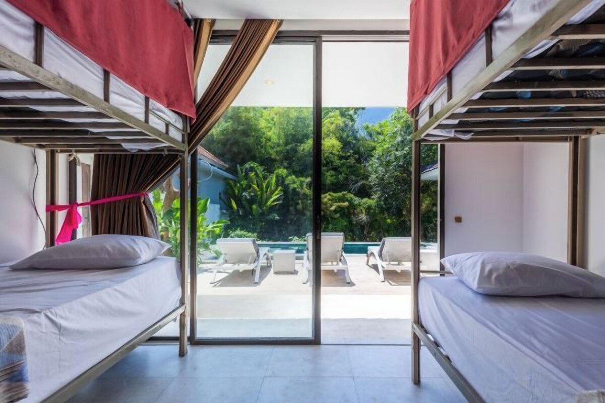 A dormitory room with bunk beds, a sliding glass door leading to an outdoor seating area.