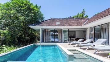 Een modern huis met een zwembad, lounge stoelen en een glazen patio.