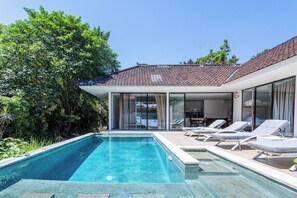 Una casa moderna con piscina, sedie a sdraio e patio in vetro.