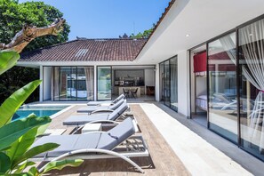 Eine moderne Villa mit Swimmingpool, Liegestühlen und einem wintergartenartigen Essbereich.