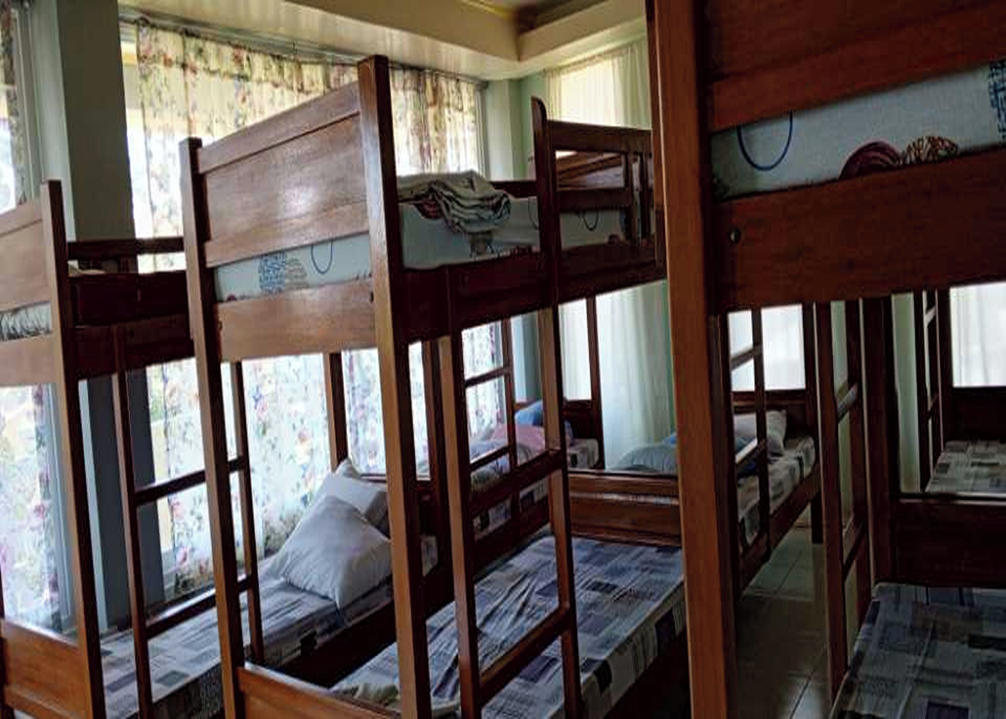 A room with bunk beds, a window with floral curtains, and a bed with a pillow.