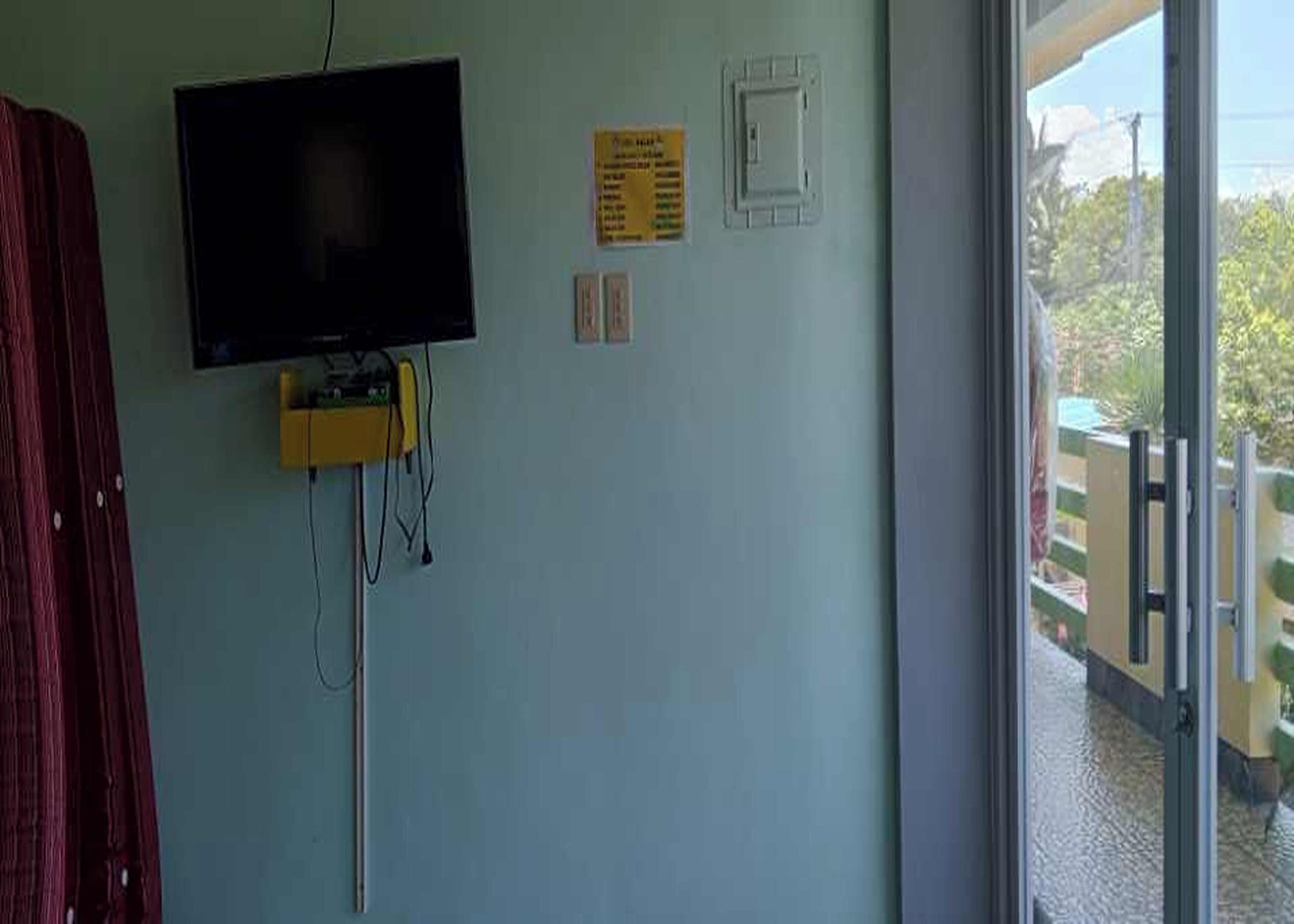 Une pièce avec un téléviseur fixé au mur, un petit appareil jaune et une fenêtre donnant sur un paysage verdoyant.