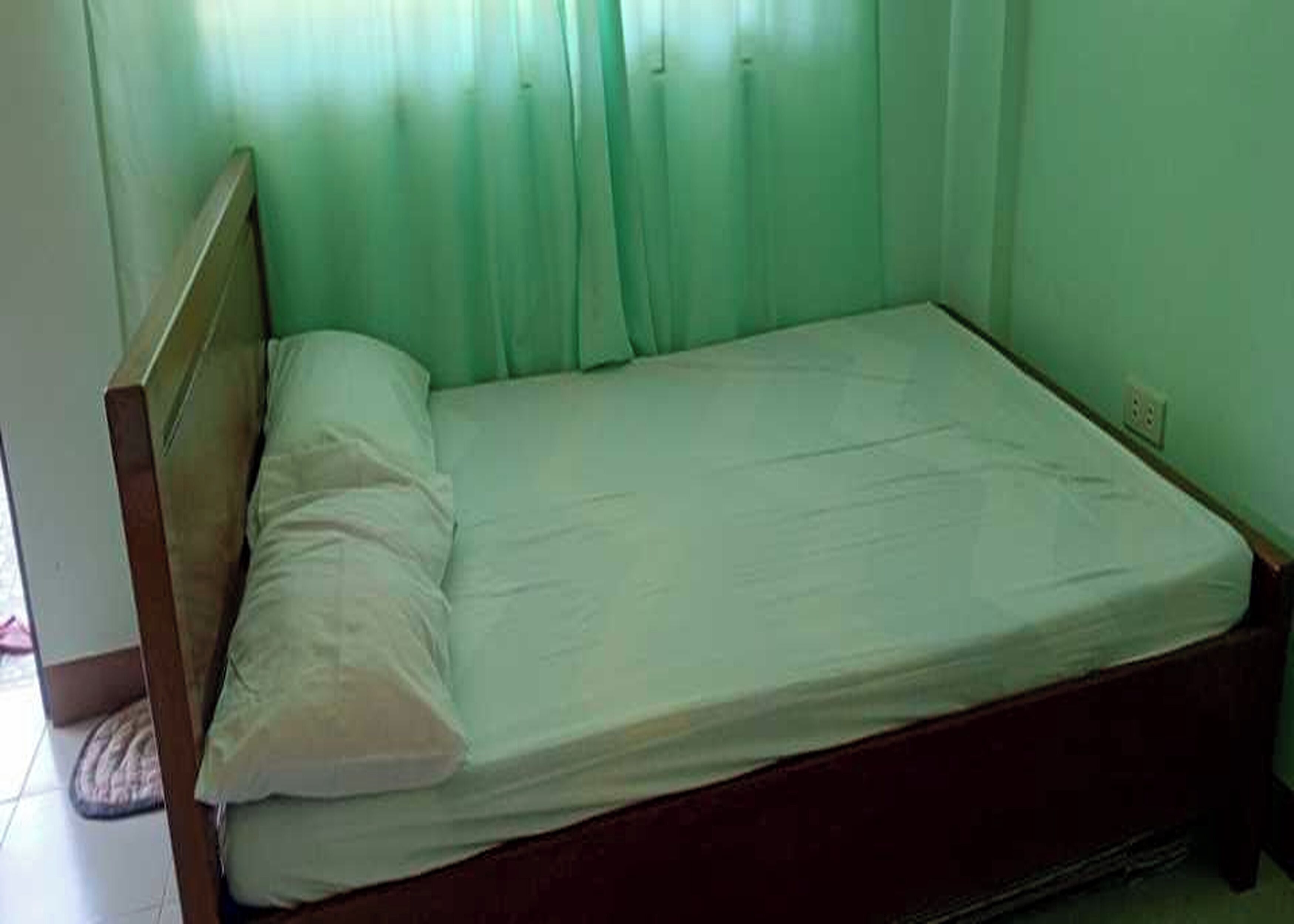 A single bed with a wooden headboard and a white mattress in a room with green walls and curtains.