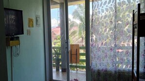 A room with a tiled floor, a television mounted on the wall, and a sliding glass door leading to an outdoor area with a wooden chair and a potted plant. - Awel Seashore Inn Baler (Baler)