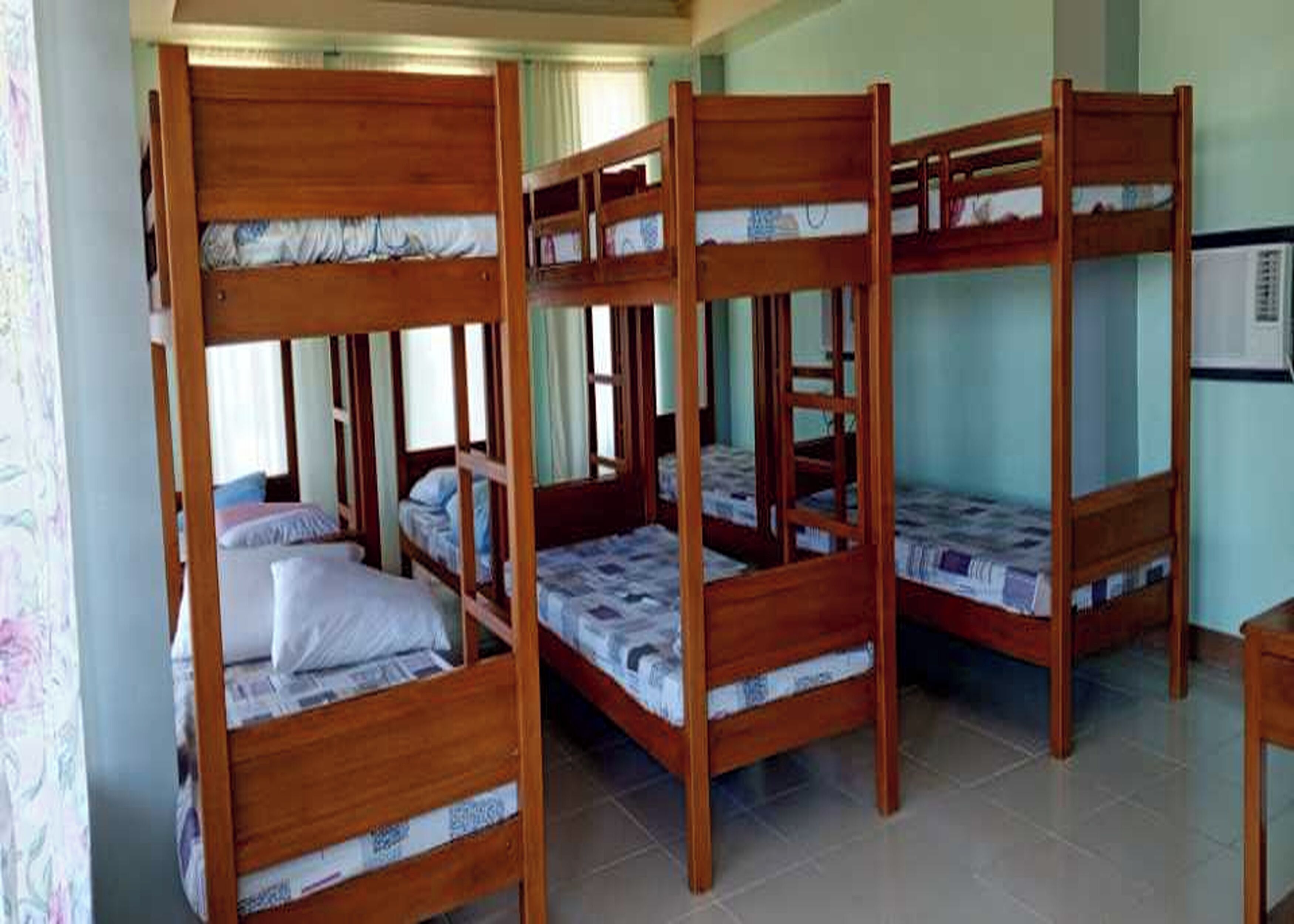 A room with four wooden bunk beds, each with a mattress and pillows.