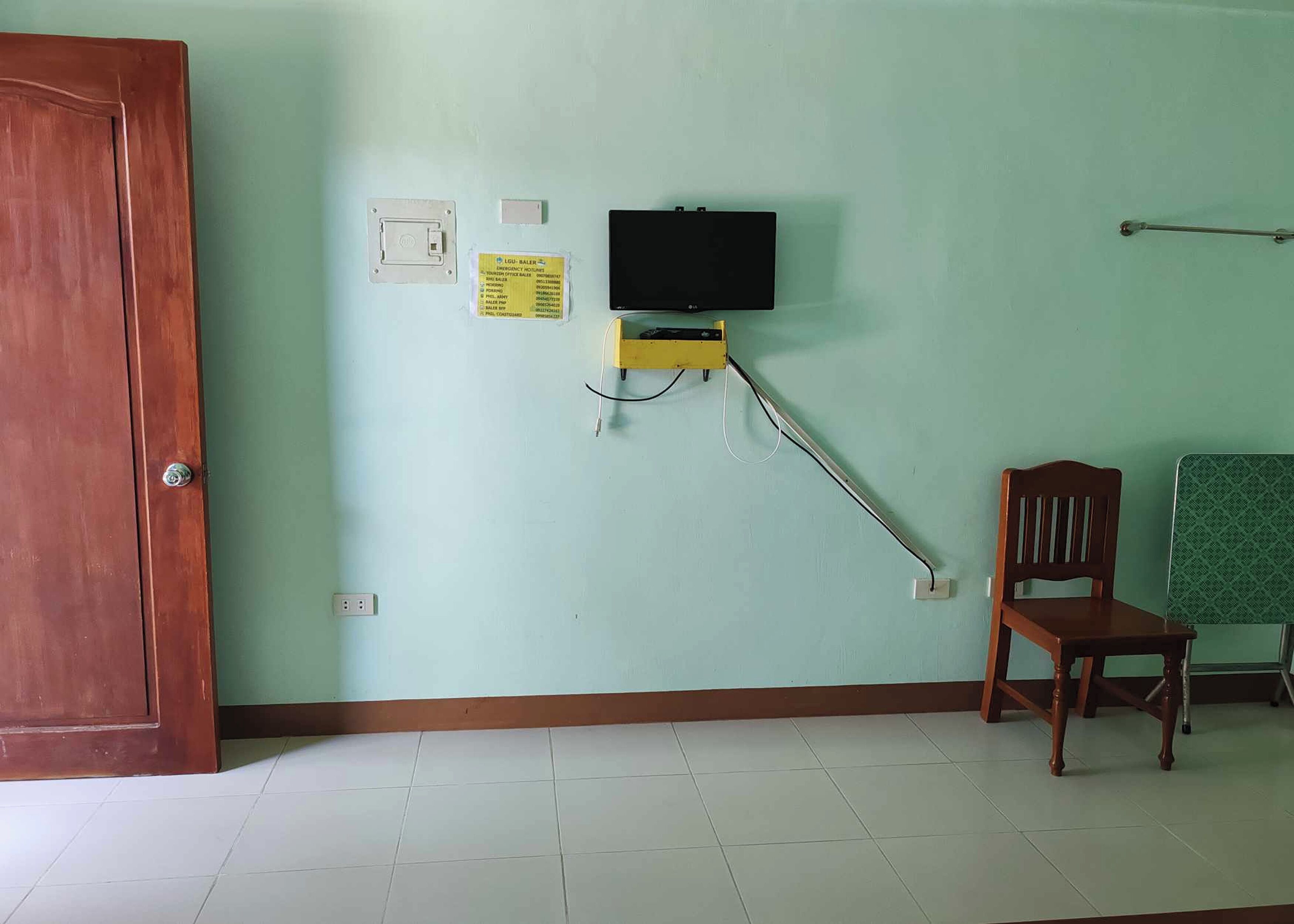 A room with a wooden door, a television mounted on the wall, a chair, and a small table.