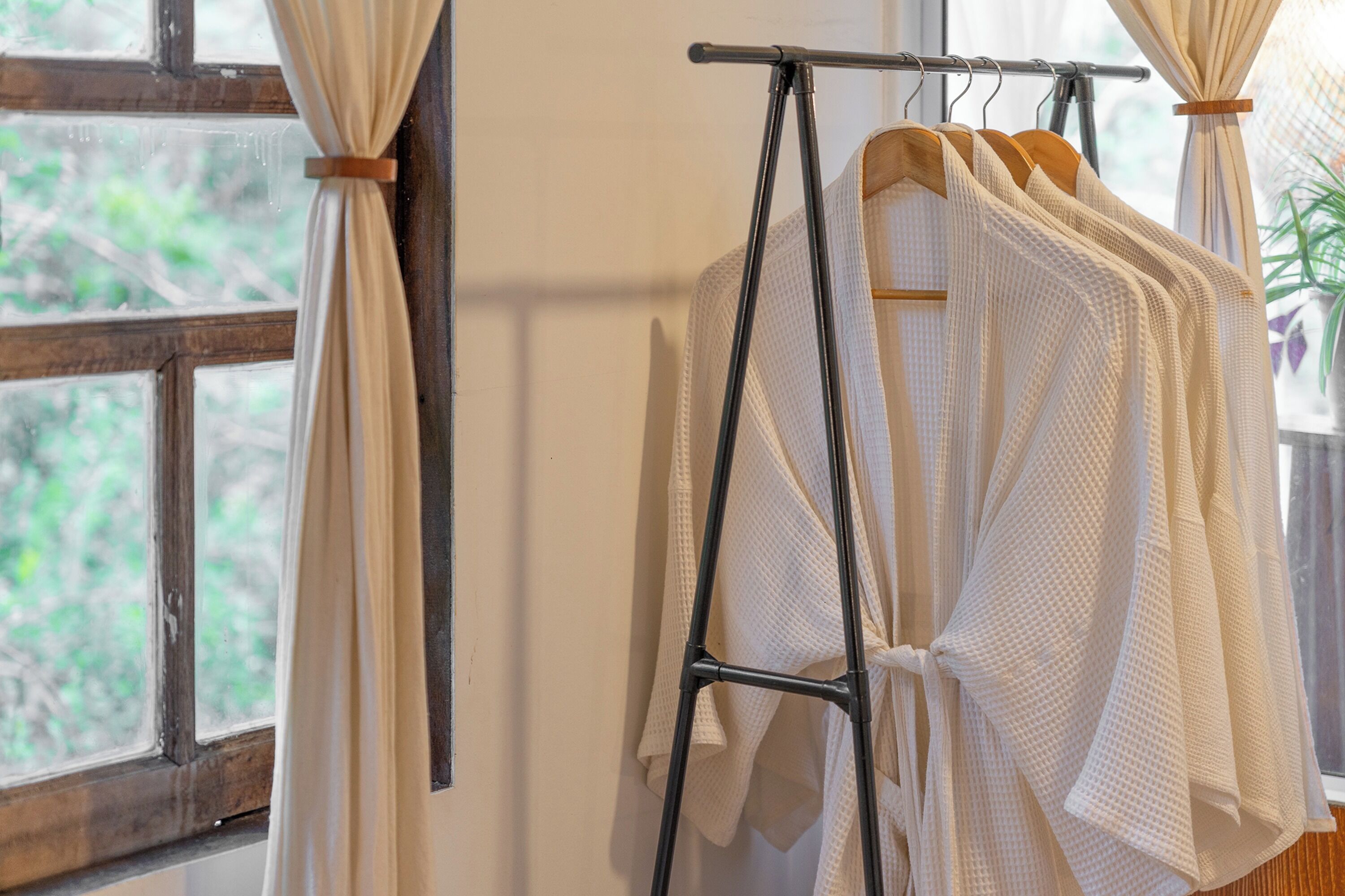 A rack with white robes hanging in a room with a window.