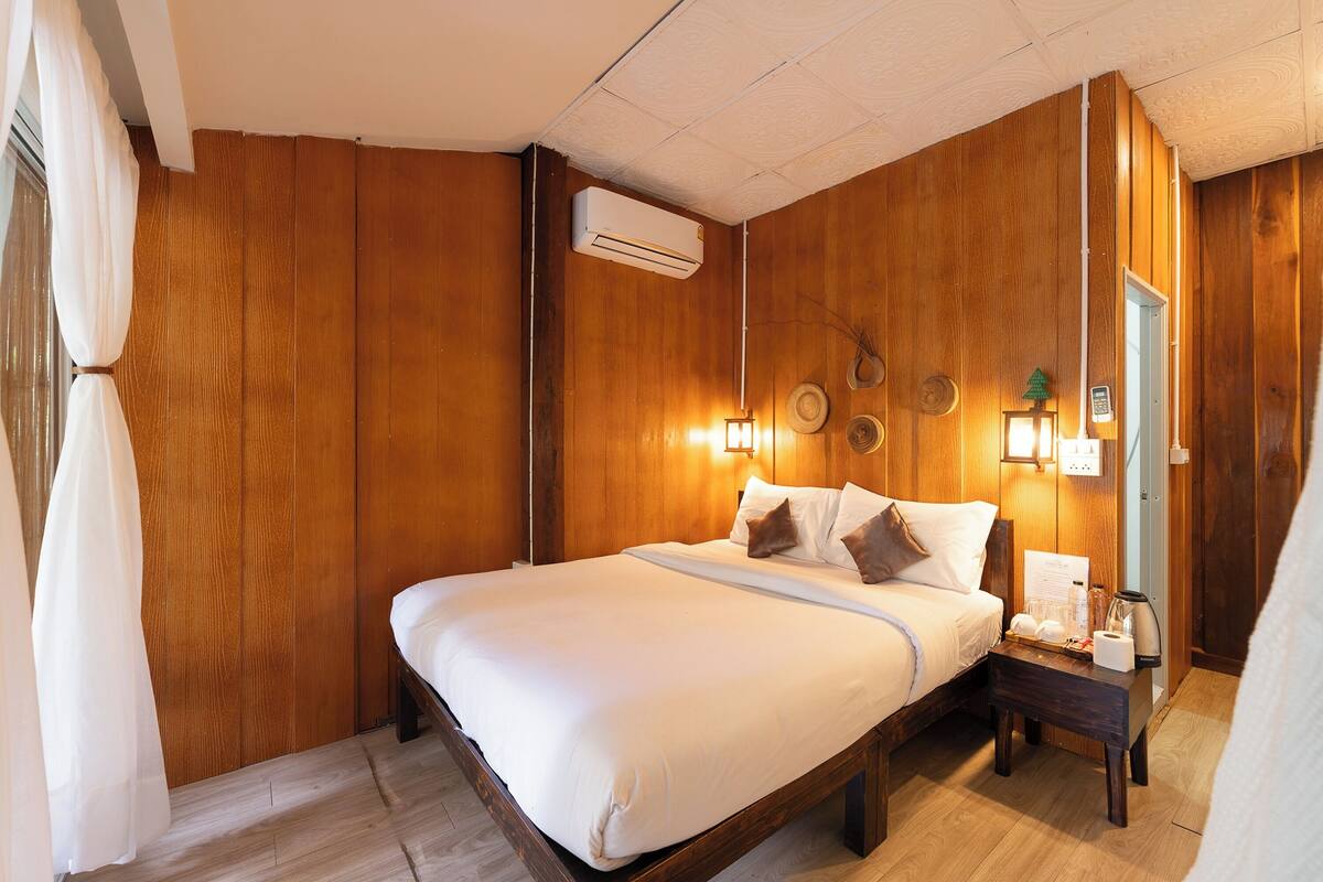 Une chambre d’hôtel avec un mur lambrissé en bois, un lit avec du linge de maison blanc, une table de chevet avec une lampe et un appareil de climatisation.