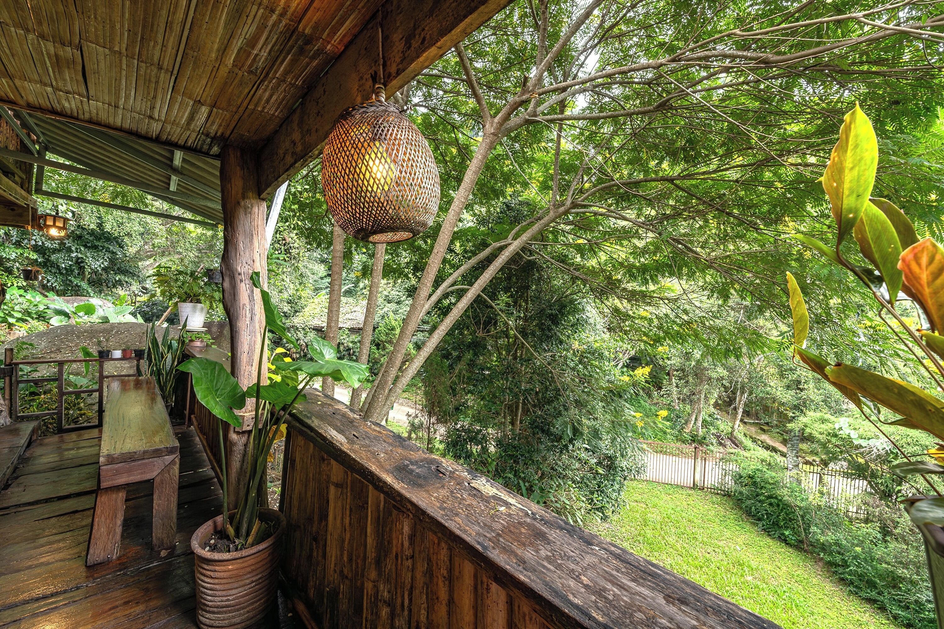 Una terraza de madera con un banco, una lámpara colgante y una planta en maceta.