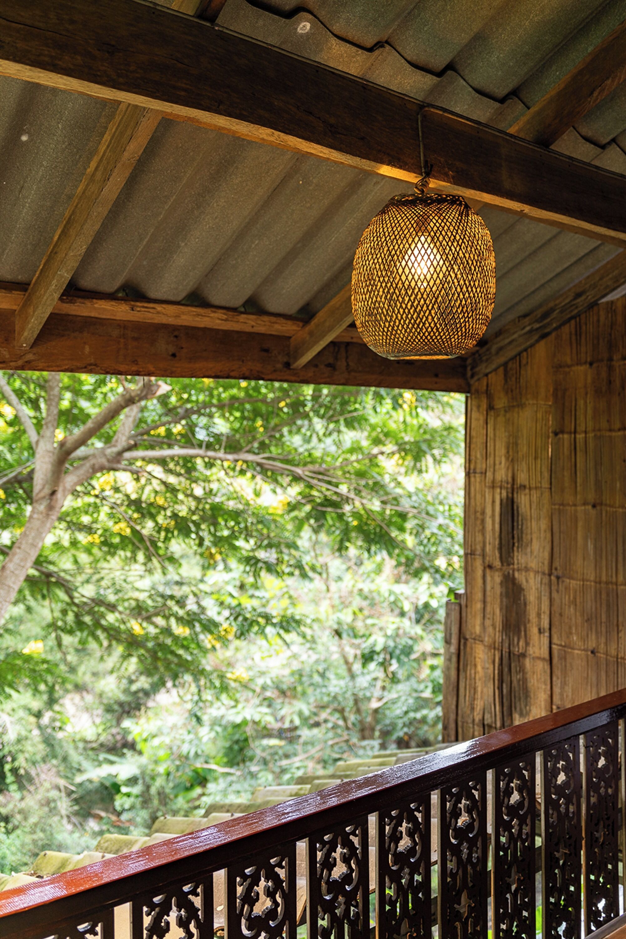 A wooden staircase with intricate railing design, leading to an outdoor area with a view of lush greenery.