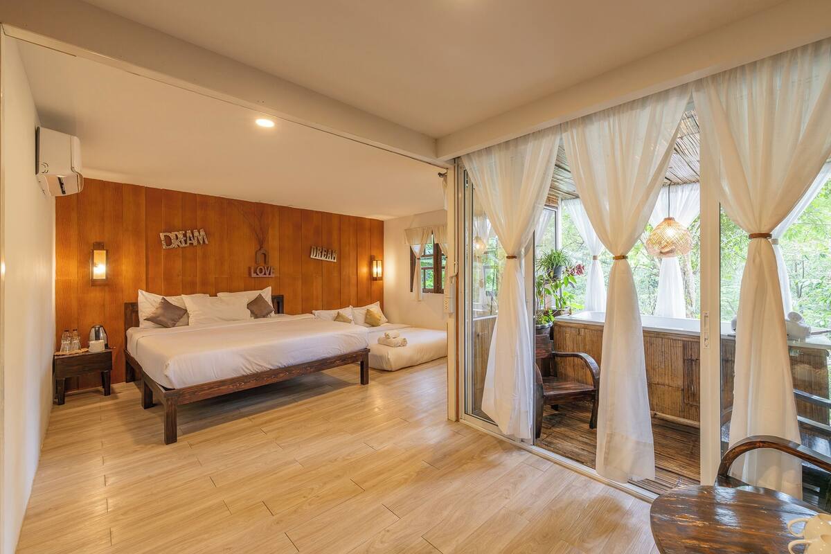 Une chambre à coucher avec une tête de lit en bois, un grand lit, une table de chevet et une fenêtre ornée de rideaux légers.