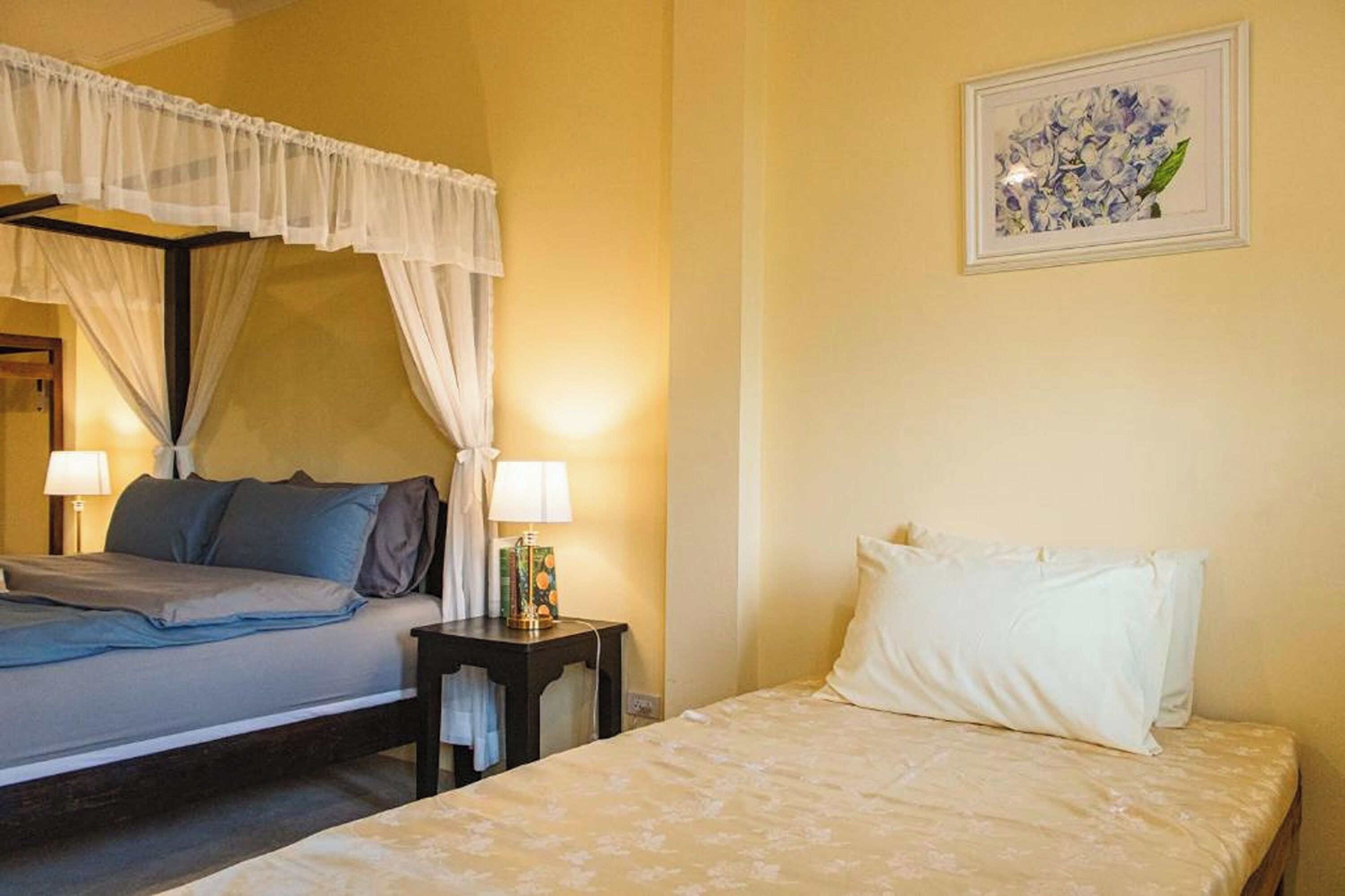 A hotel room with a bed, bedside table, lamp, and a framed picture on the wall.