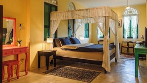A bedroom with a four-poster bed, a bedside table with a lamp, a desk, and a chair. - Bhirom At Baan Thongjaya (Hang Dong)
