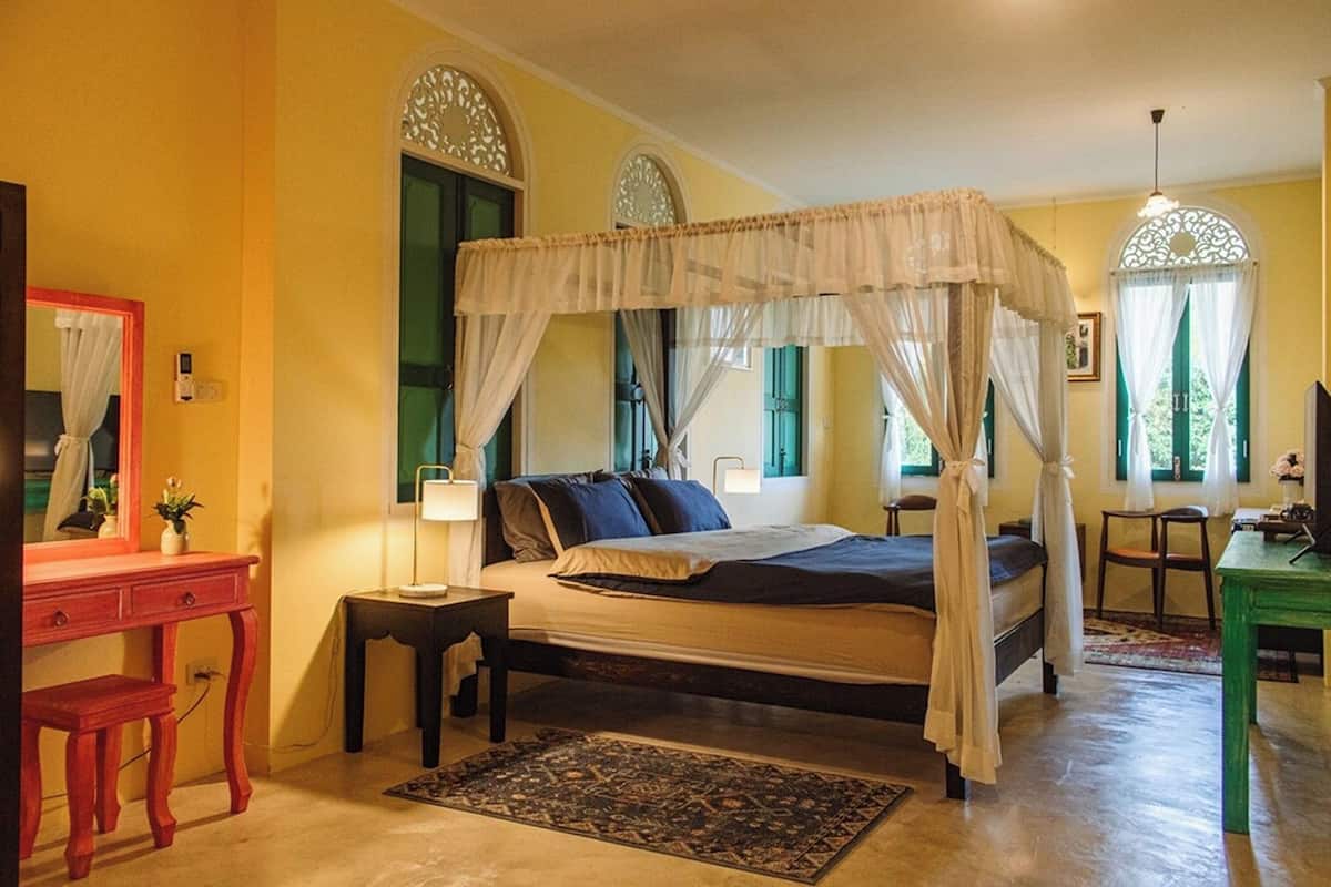 A bedroom with a four-poster bed, a bedside table with a lamp, a desk, and a chair.