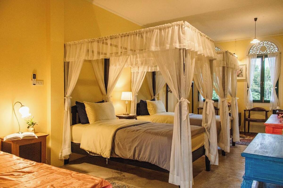 A room with four beds, each with a canopy, and a small table with a lamp.