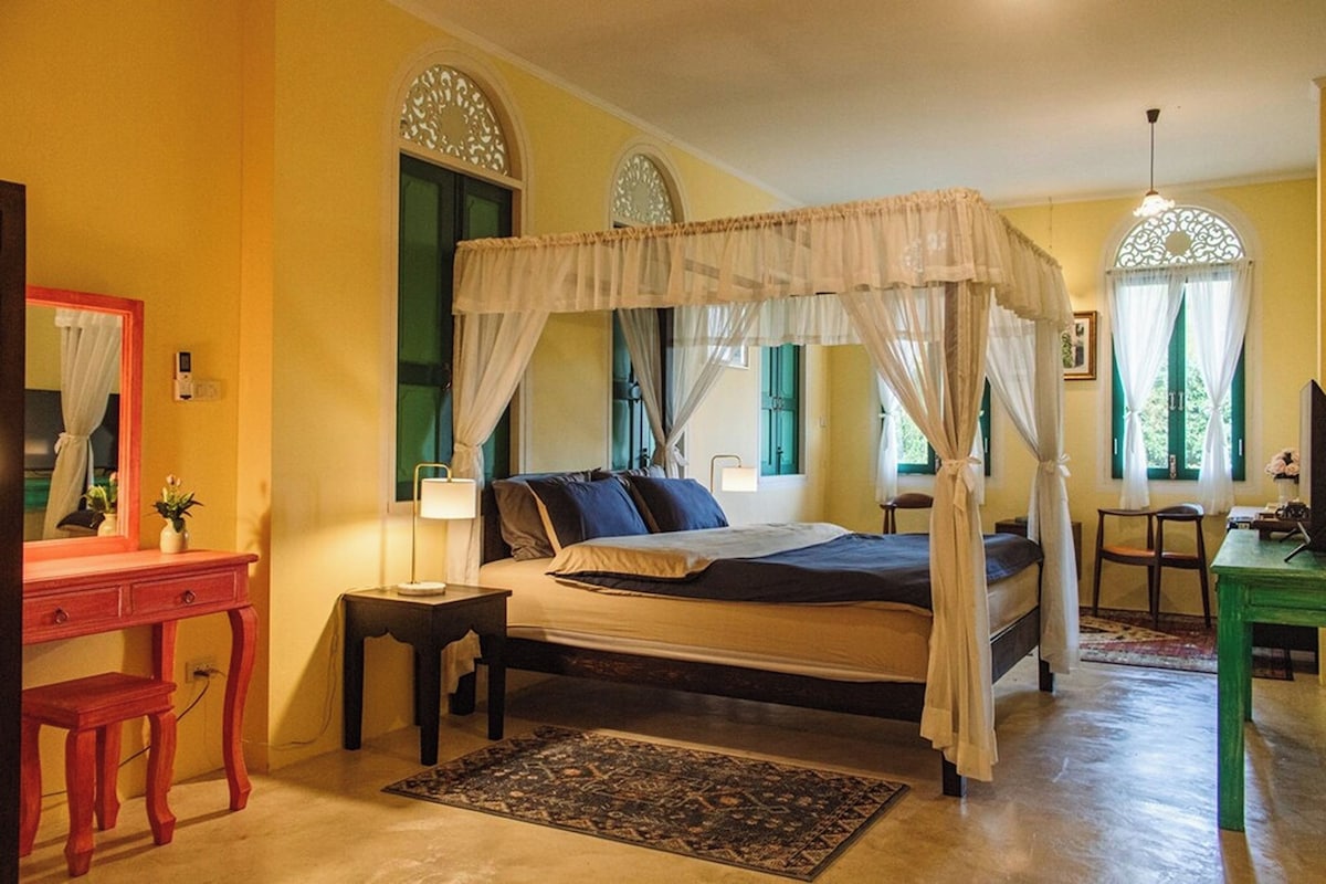 A bedroom with a four-poster bed, a nightstand, a desk, and a mirror.