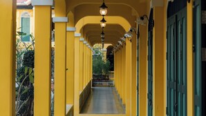 A corridor with yellow walls and a wooden floor, leading to a door with a green frame. - Bhirom At Baan Thongjaya (Hang Dong)