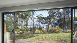 Un interior moderno con grandes puertas de cristal que dan a una terraza exterior con vistas a un área verde y árboles.