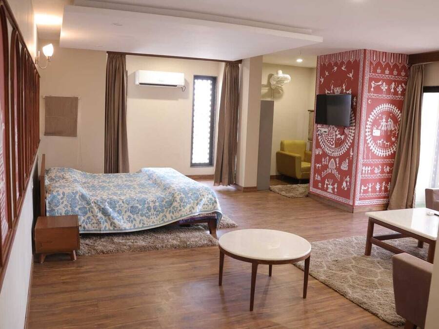 Habitación de hotel con cama, una mesa redonda, sofá, televisor y pared con estampado rojo.