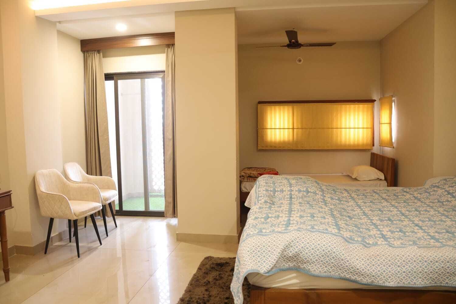 A hotel room with a bed, a chair, a desk, and a sliding glass door leading to a balcony.