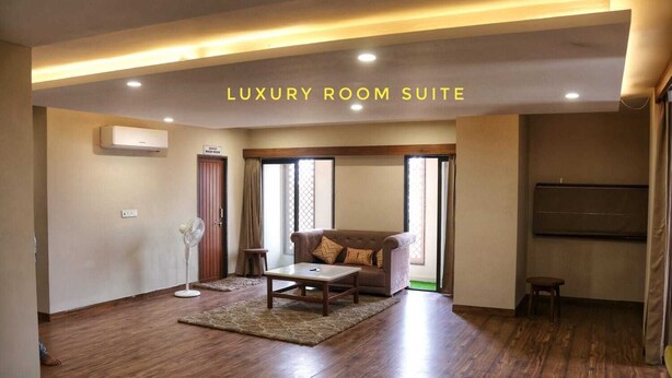 A luxury room suite with a sofa, coffee table, and a flat-screen TV. - Devraha Seva Ashram - Vrindavan (Mathura)