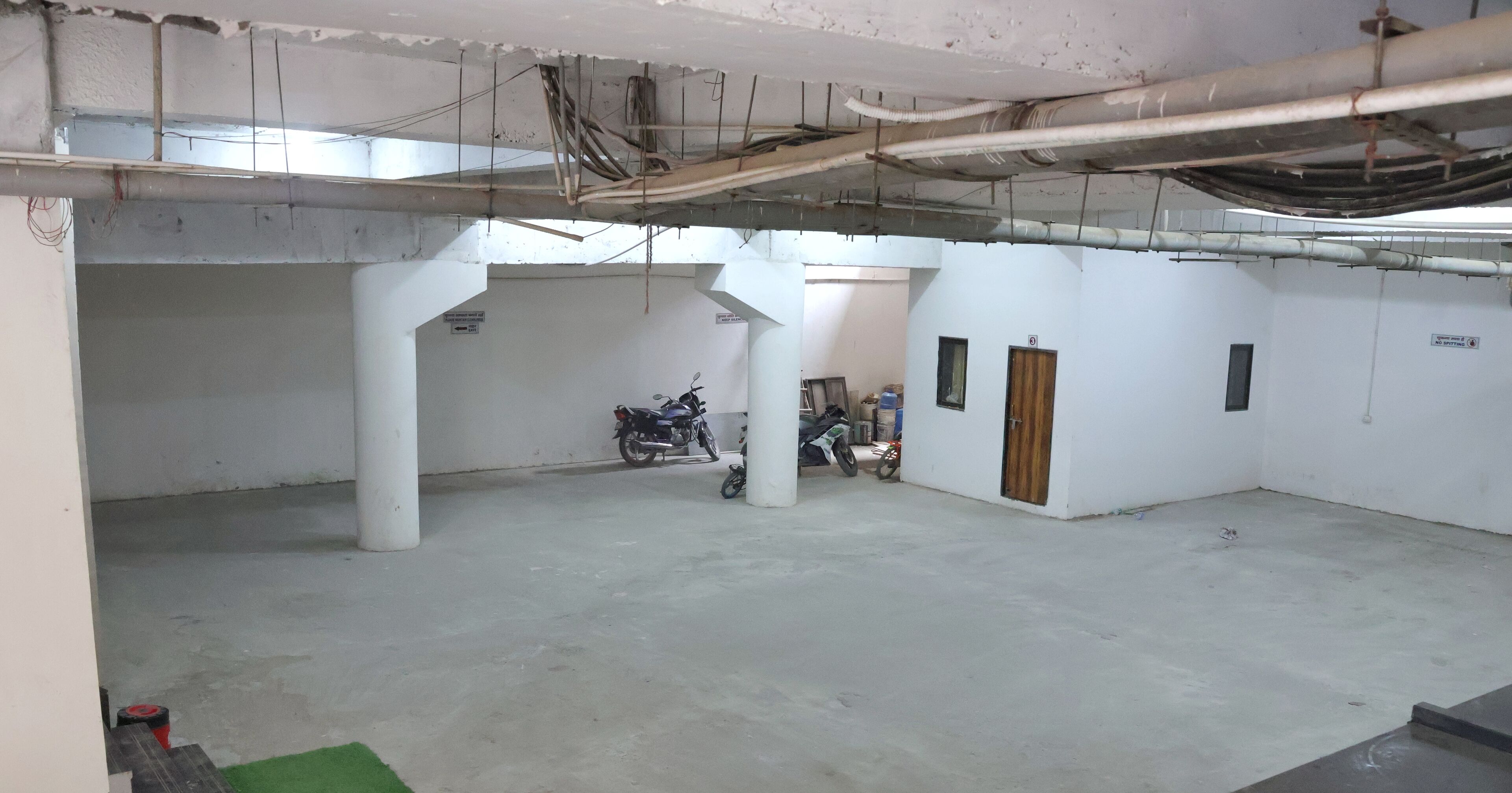 A spacious indoor area with concrete flooring, white walls, and exposed ceiling pipes.