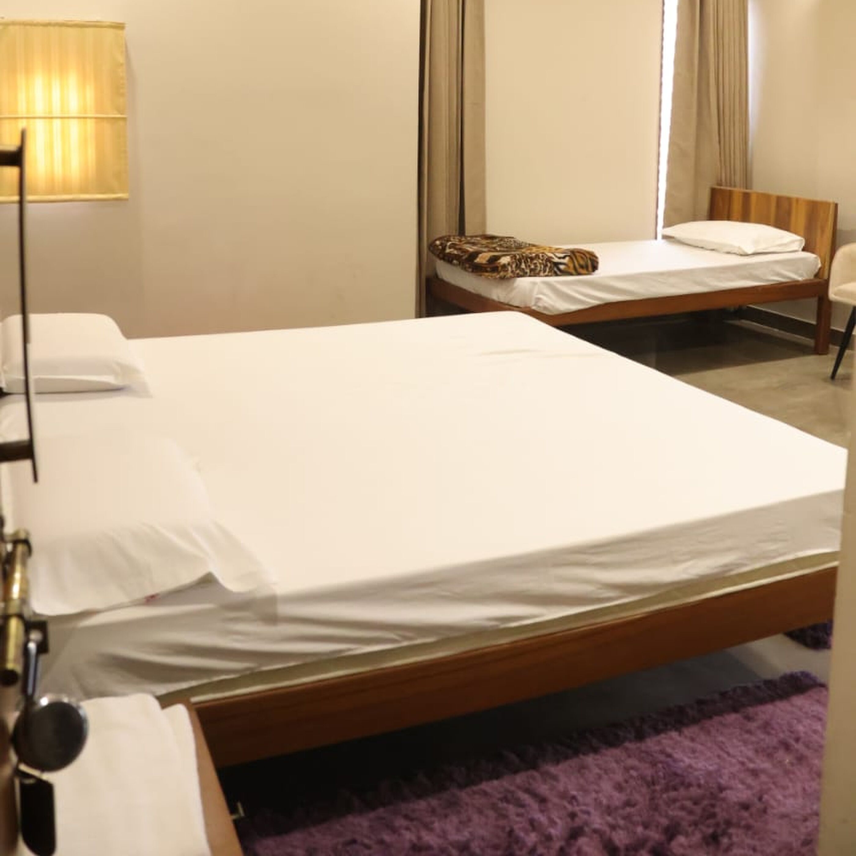 A hotel room with two single beds, a wooden headboard, a purple rug, and a lamp.