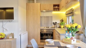 Eine kompakte Küche mit Holzausbau, fest eingebautem Backofen, Gasherd und kleinem Spülbecken. Ein Esstisch mit Stuhl steht dort, und an der Wand ist ein Fernseher befestigt.