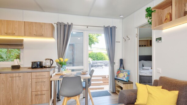 Ein kompakter Wohnraum mit Küchenzeile, Essbereich und einer Couch mit gelben Kissen.