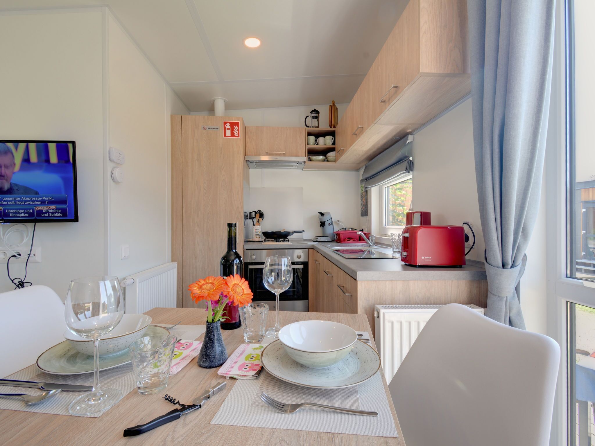 A modern kitchen with wooden cabinets, a red coffee maker, and a dining area with a table set for two.