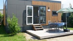 A modern, compact building with a wooden deck, a table with chairs, and an umbrella. - Tiny Haus Sonnendeck by Interhome (Beilngries)