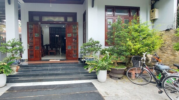 A house with a wooden door, steps leading to a porch, and potted plants. - Melody Riverside Homestay  (Hue)