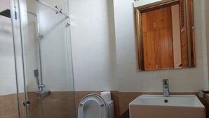 A bathroom with a glass-enclosed shower, a white toilet, and a sink with a mirror above it. - Melody Riverside Homestay  (Hue)