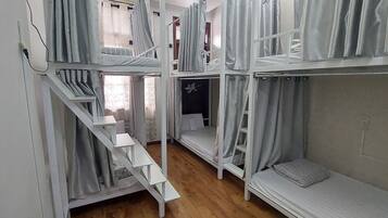 A dormitory-style room with bunk beds, a staircase, and a small window with curtains.