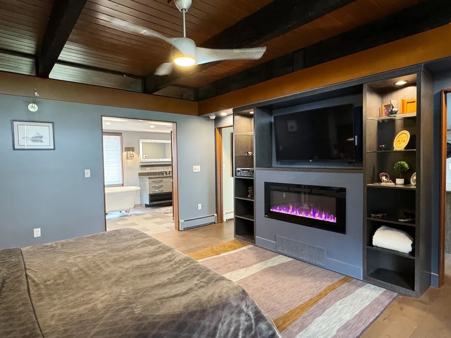 A modern living room with a fireplace, entertainment unit, and a large bed.