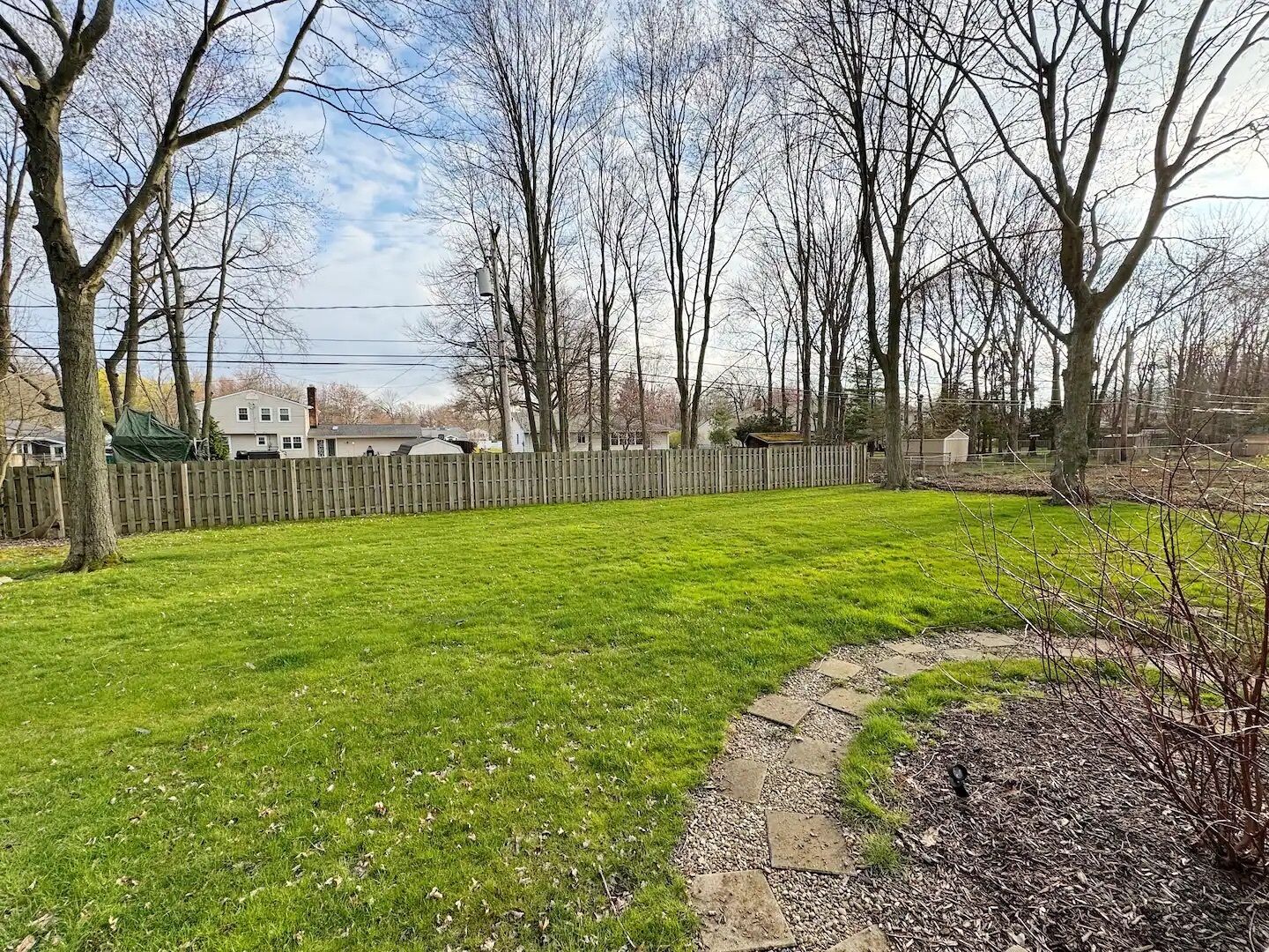 A grassy yard with a wooden fence, trees, and a stone pathway.