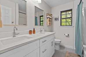A bathroom with a white sink, two mirrors, a toilet, and a window with a view of trees. - Big family friendly, Deck, Pool Table, Propane Grill & Fire Pit! (Hot Springs)