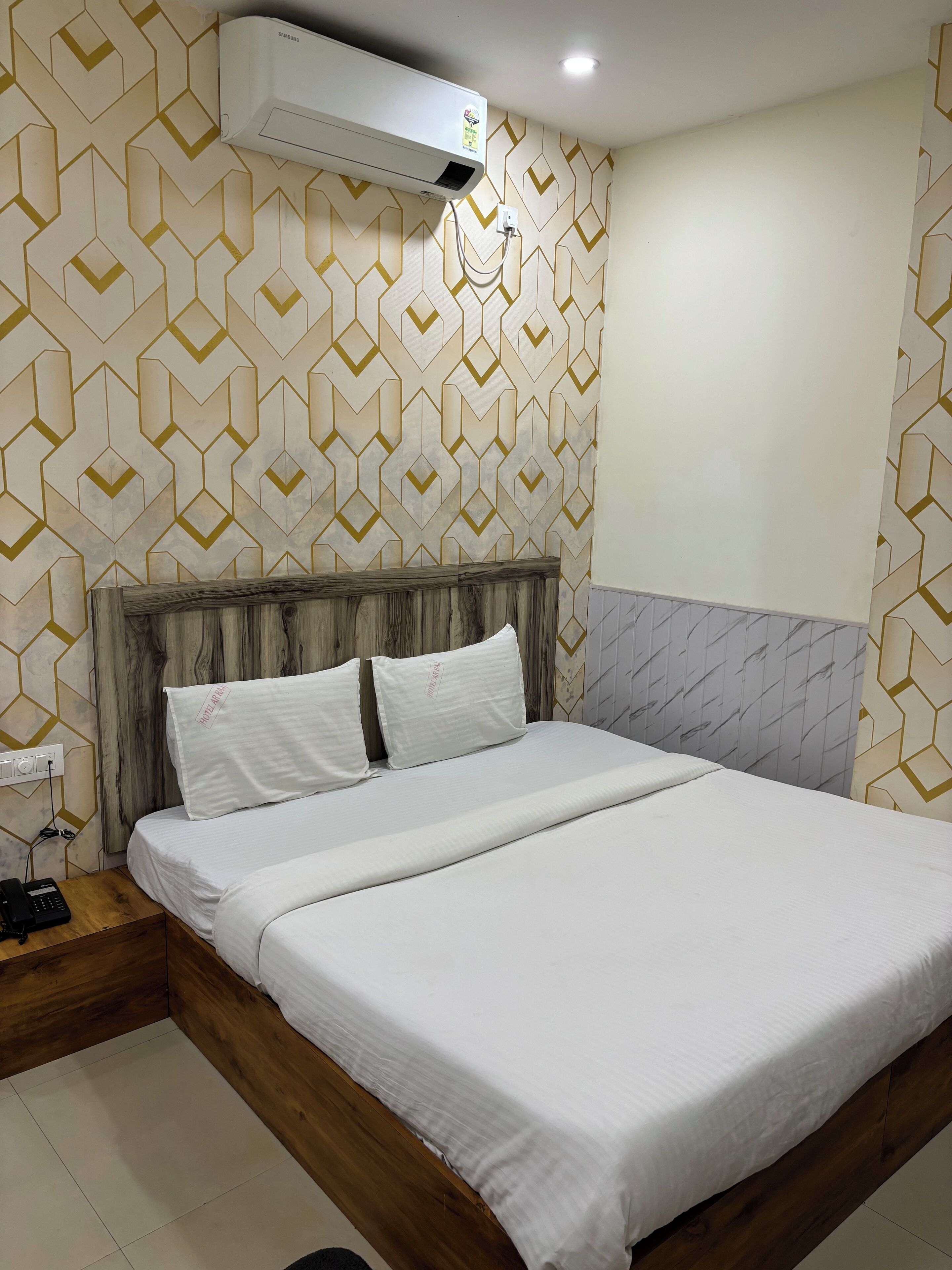 Habitación de hotel con cama, cabecero de madera y papel tapiz estampado.