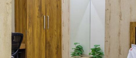 Un dormitorio con cama, armario de madera, escritorio con silla y dos plantas en macetas.